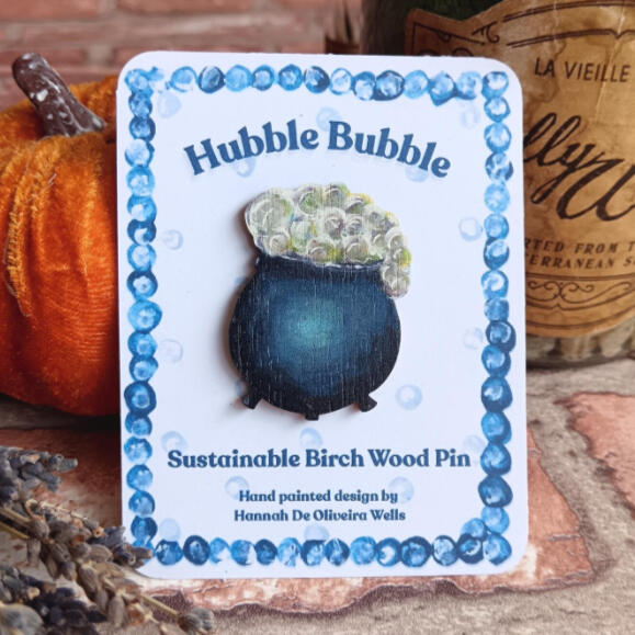 A sustainably made birchwood pin of a bubbling cauldron illustration.