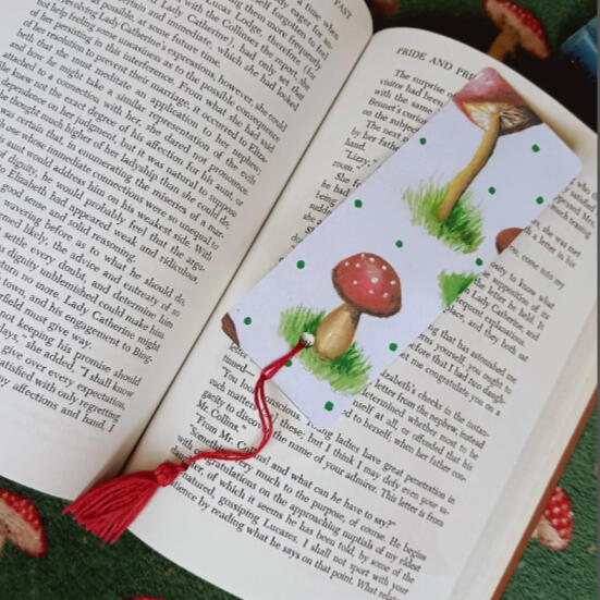 A bookmark covered in whimsical red capped mushrooms painted in acrylics and watercolours.