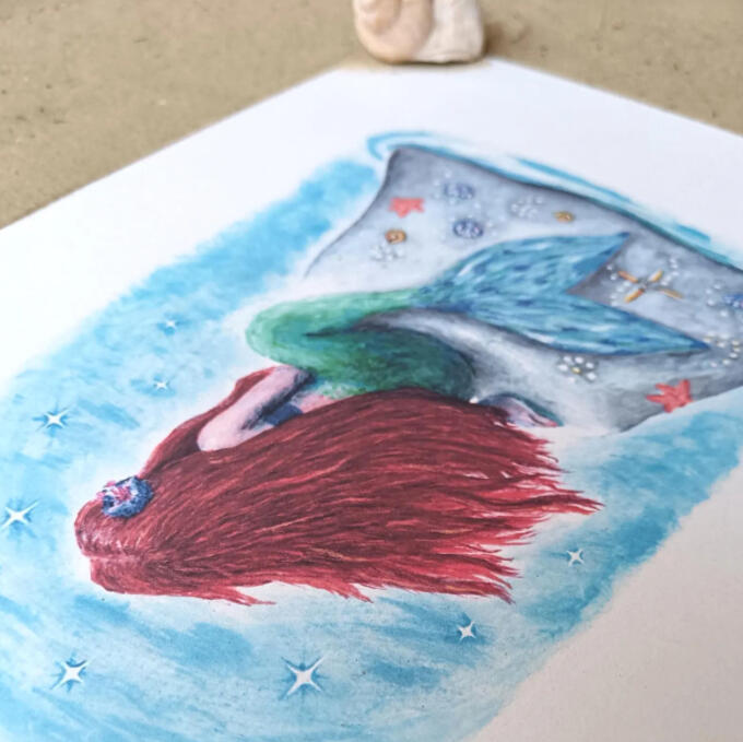 A printed illustration of a red headed mermaid looking out to sea.